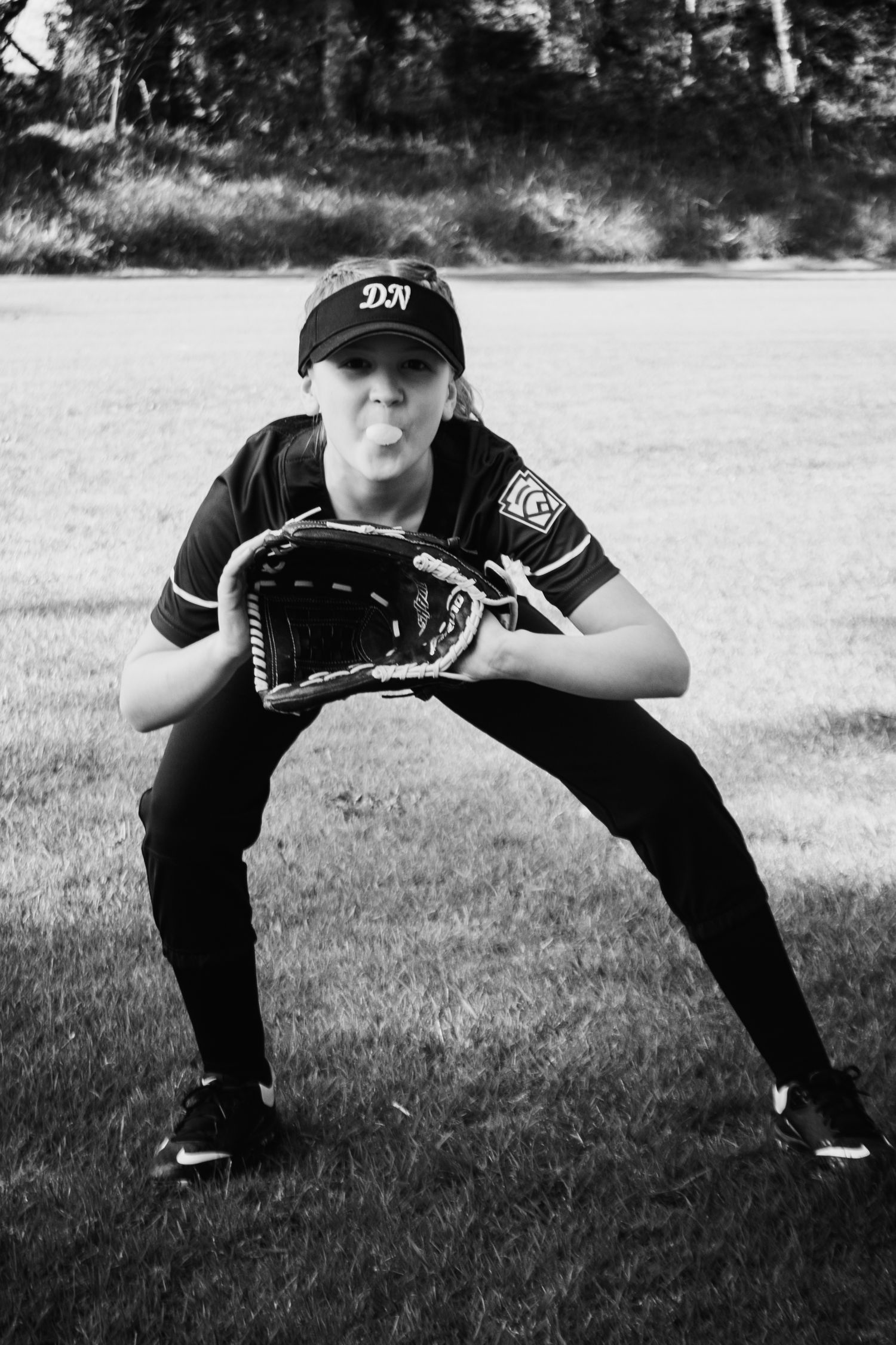Black and white photo of female softball player in fielding stance with glove on grass field.