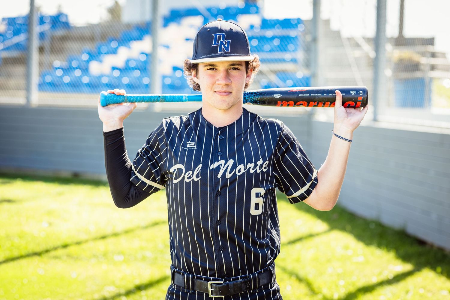 Del Norte baseball player #6 in pinstripe uniform holding bat across shoulders outdoors.