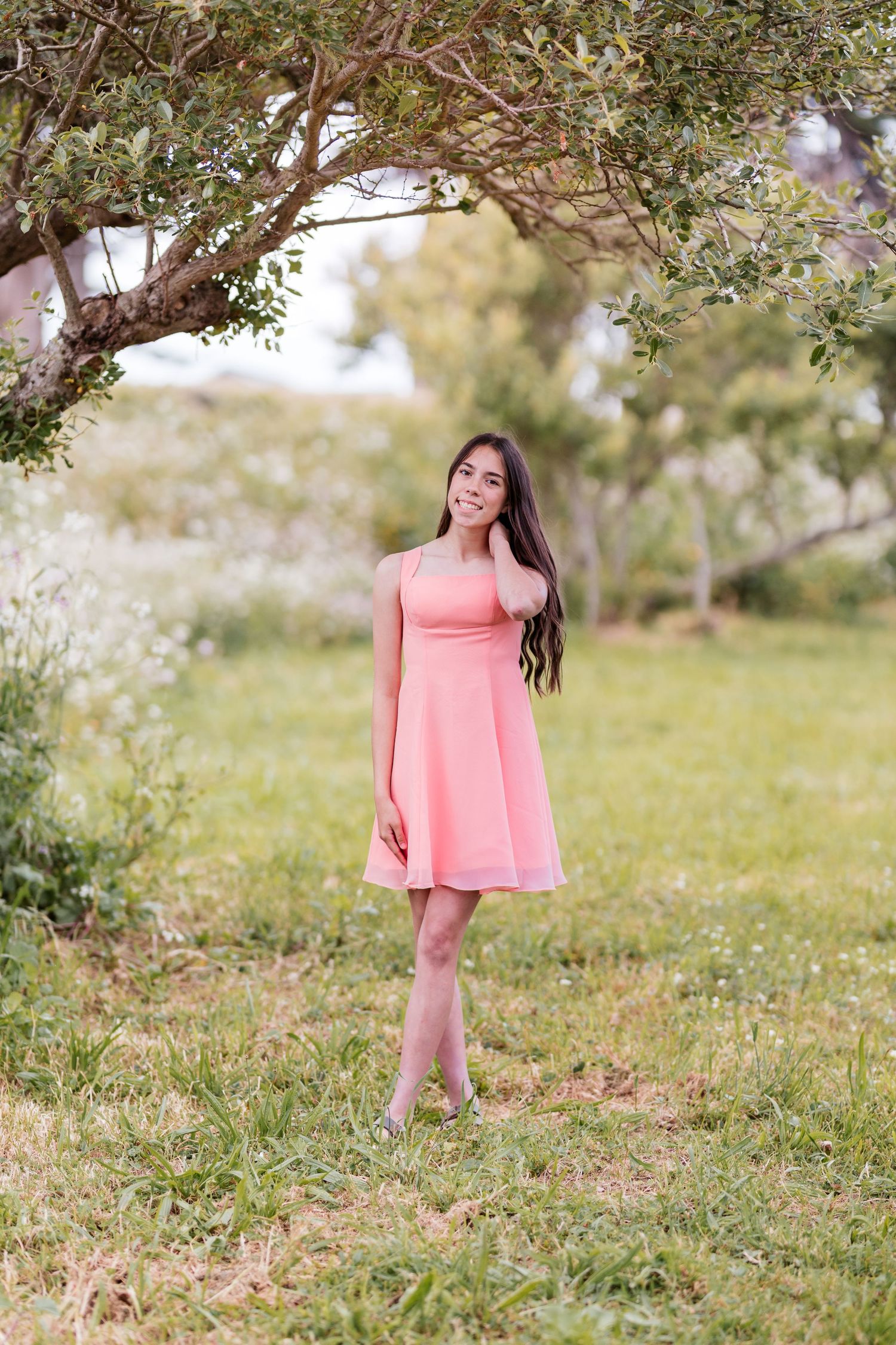 Young woman in pink dress standing barefoot on green grass under a tree in a serene outdoor setting.