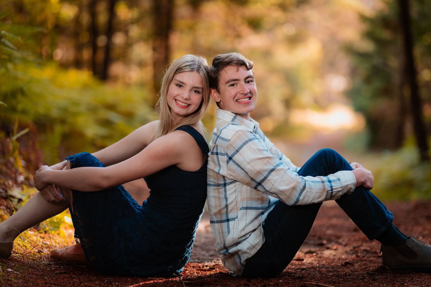 Young couple sitting back-to-back smiling in a colorful autumn forest setting.