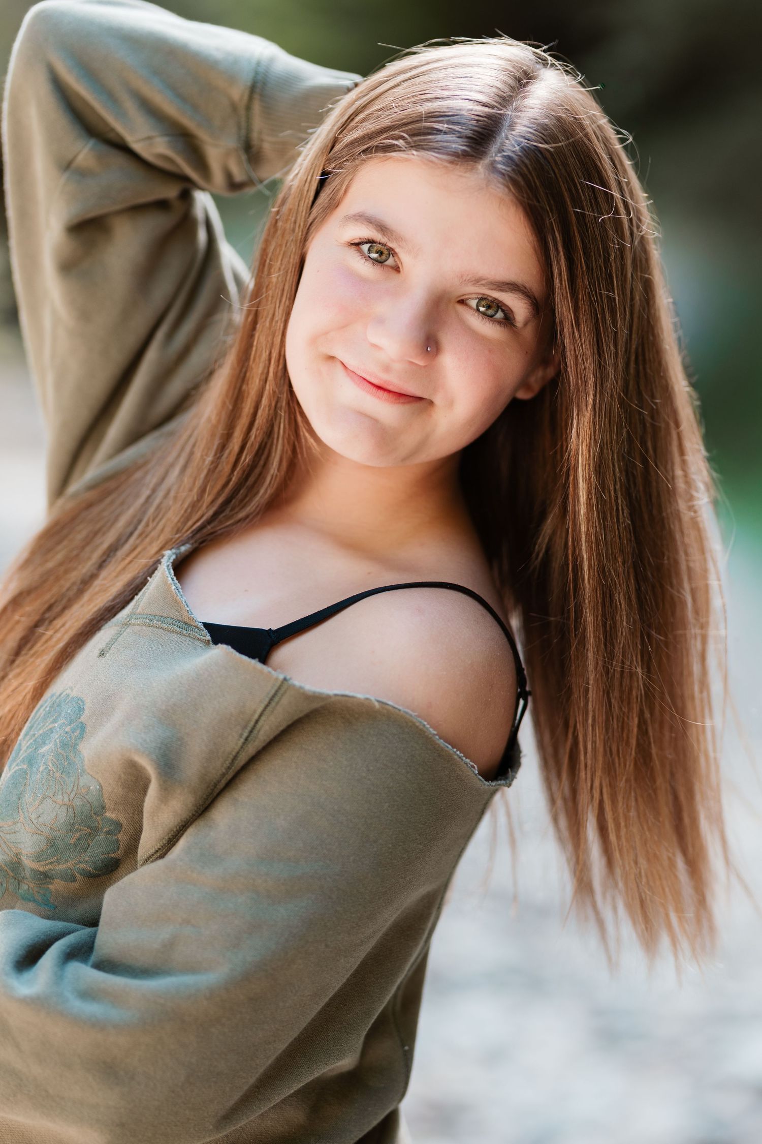 Young teen girl with long brown hair smiling outdoors in olive green off-shoulder top.