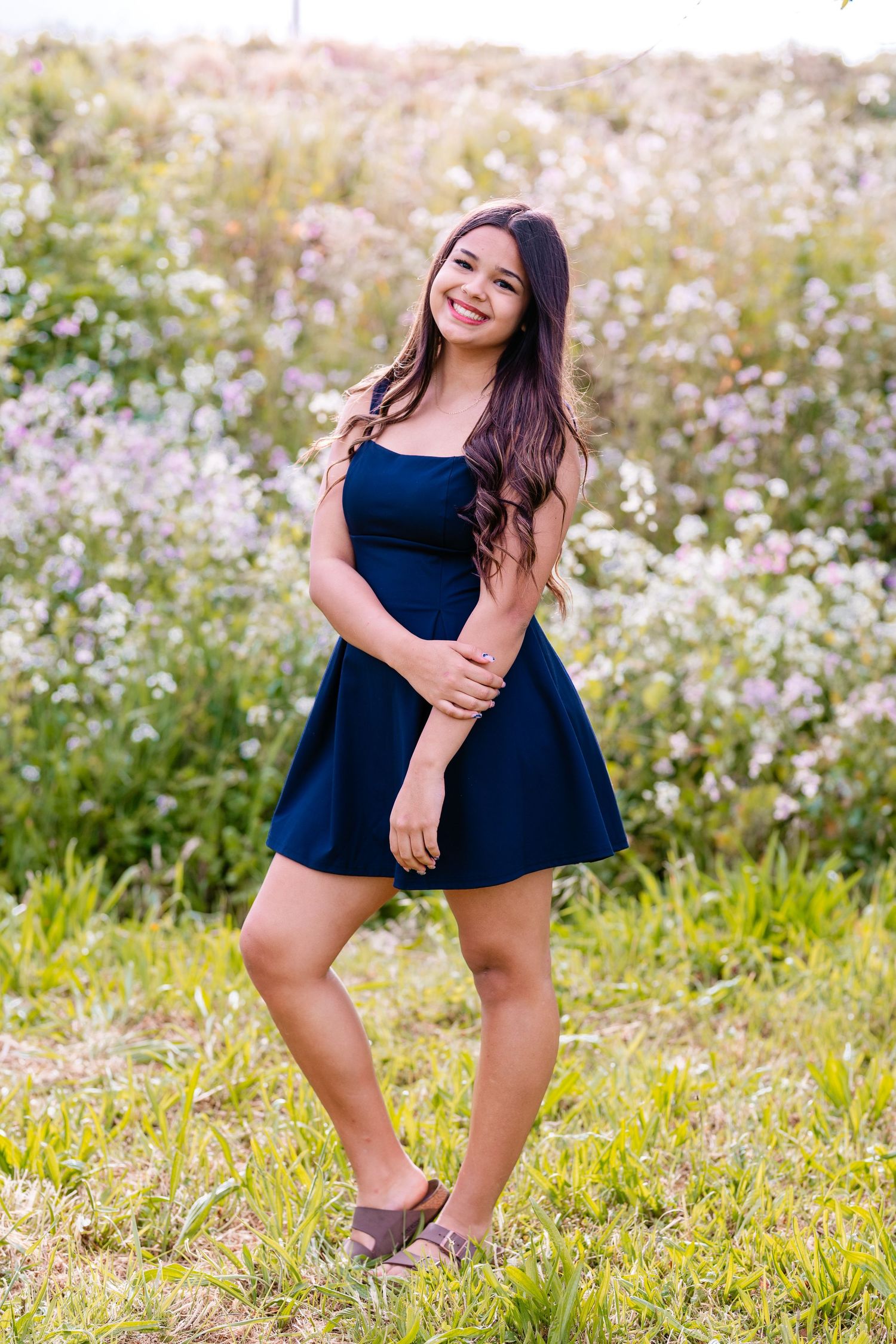 Young woman in navy blue dress smiling in a wildflower field.