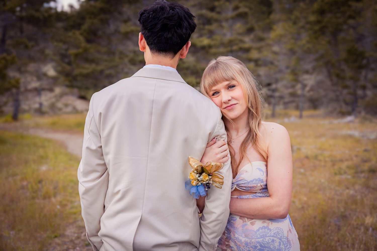 Young couple in formal attire embracing outdoors with rocky landscape background.
