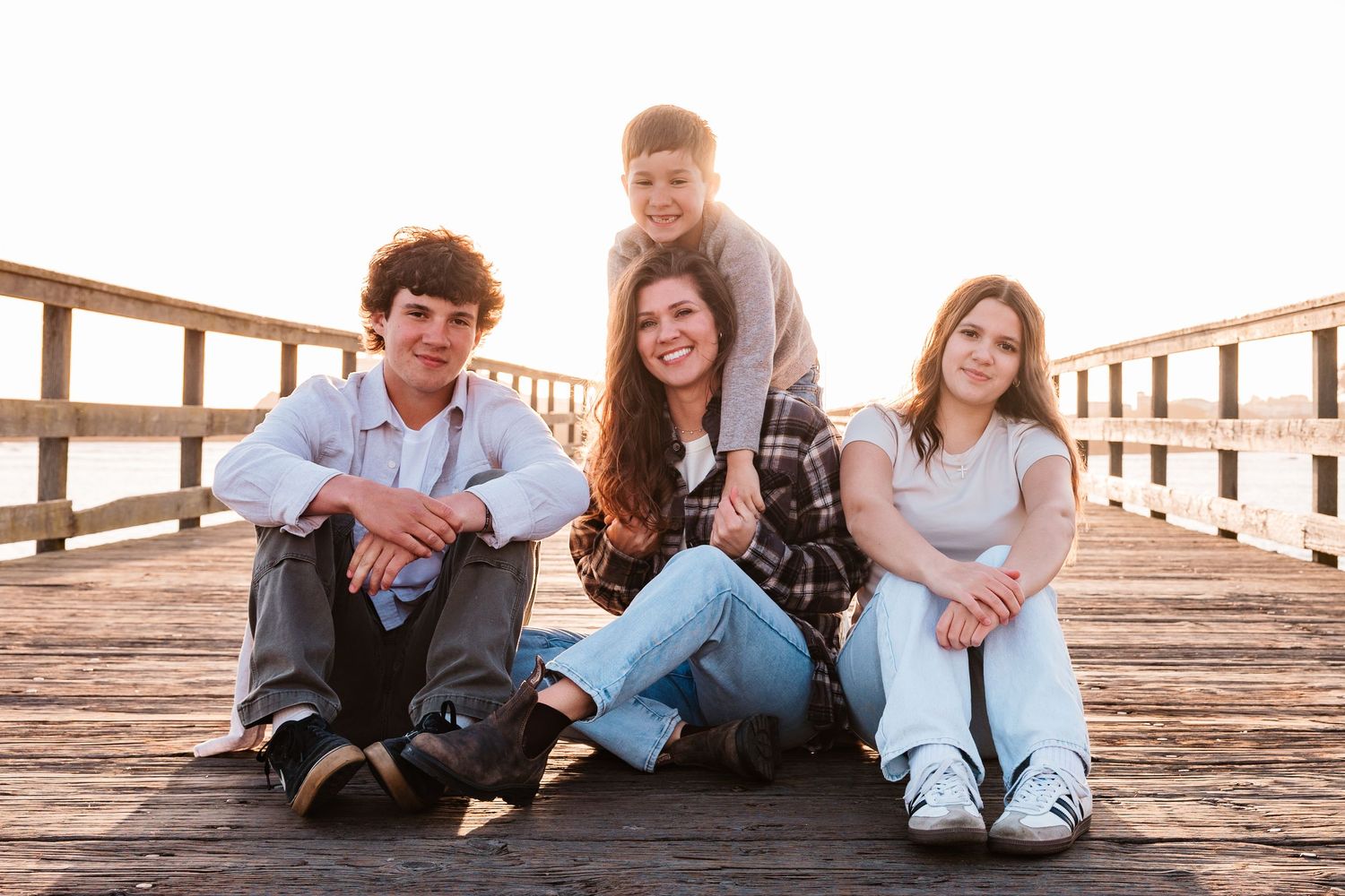 Four siblings posing together on a wooden pier boardwalk during a warm golden sunset photo session.