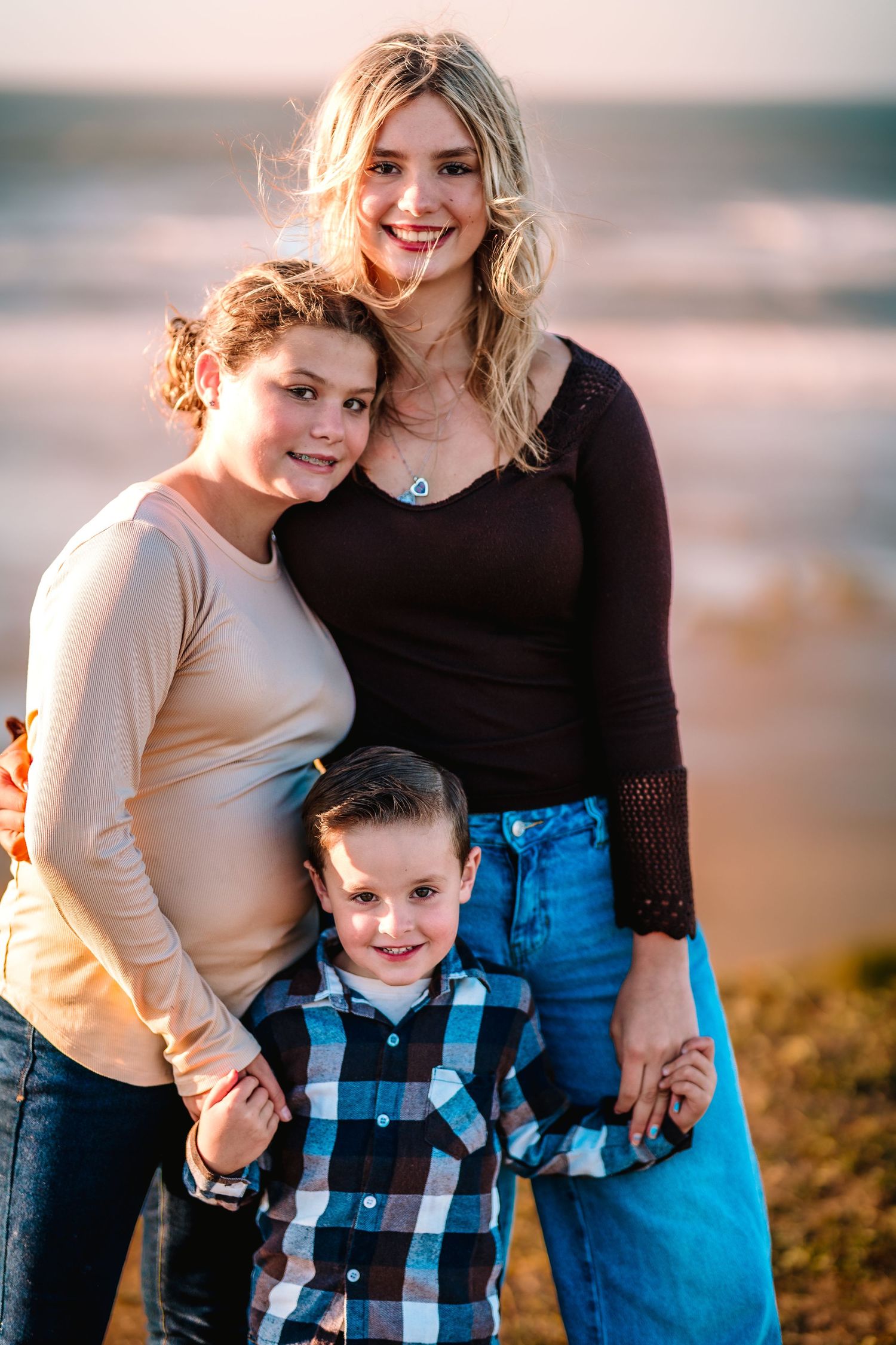 Two women and a young boy pose together on a beach at sunset, smiling warmly at the camera.