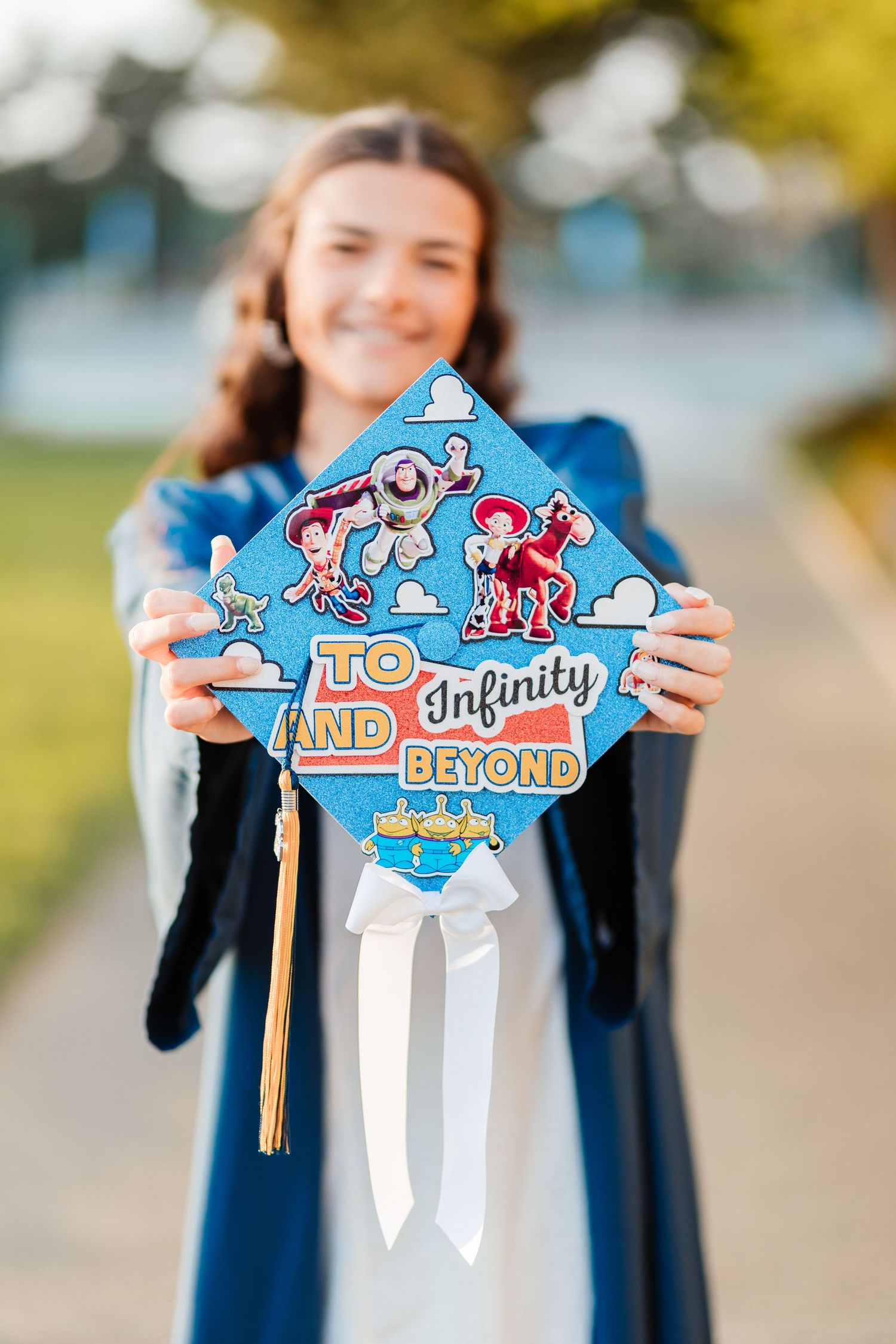 Smiling graduate holds Toy Story-themed graduation cap reading To Infinity and Beyond outdoors.