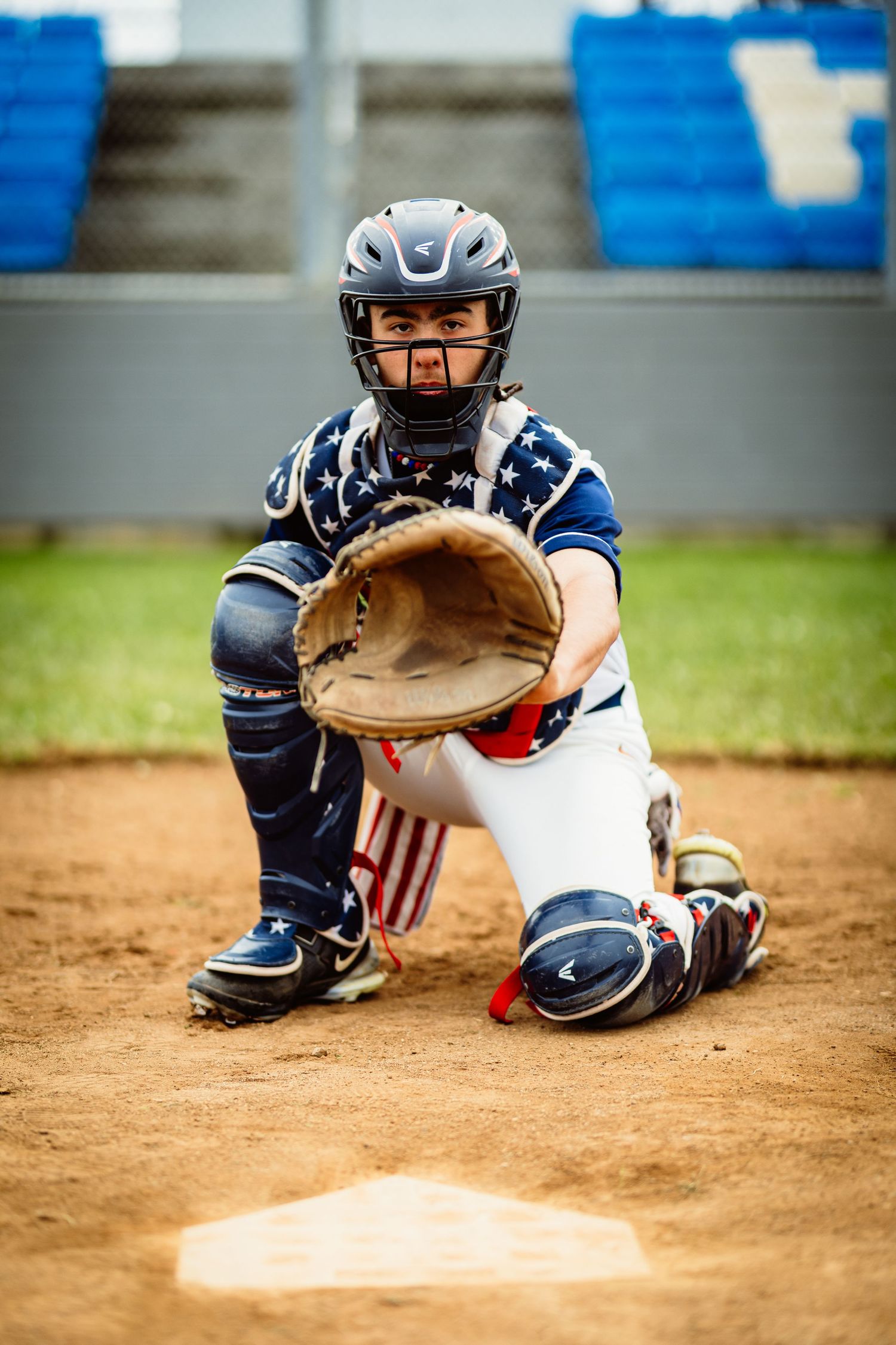 Baseball catcher in patriotic stars gear crouching at home plate with mitt open ready to catch.