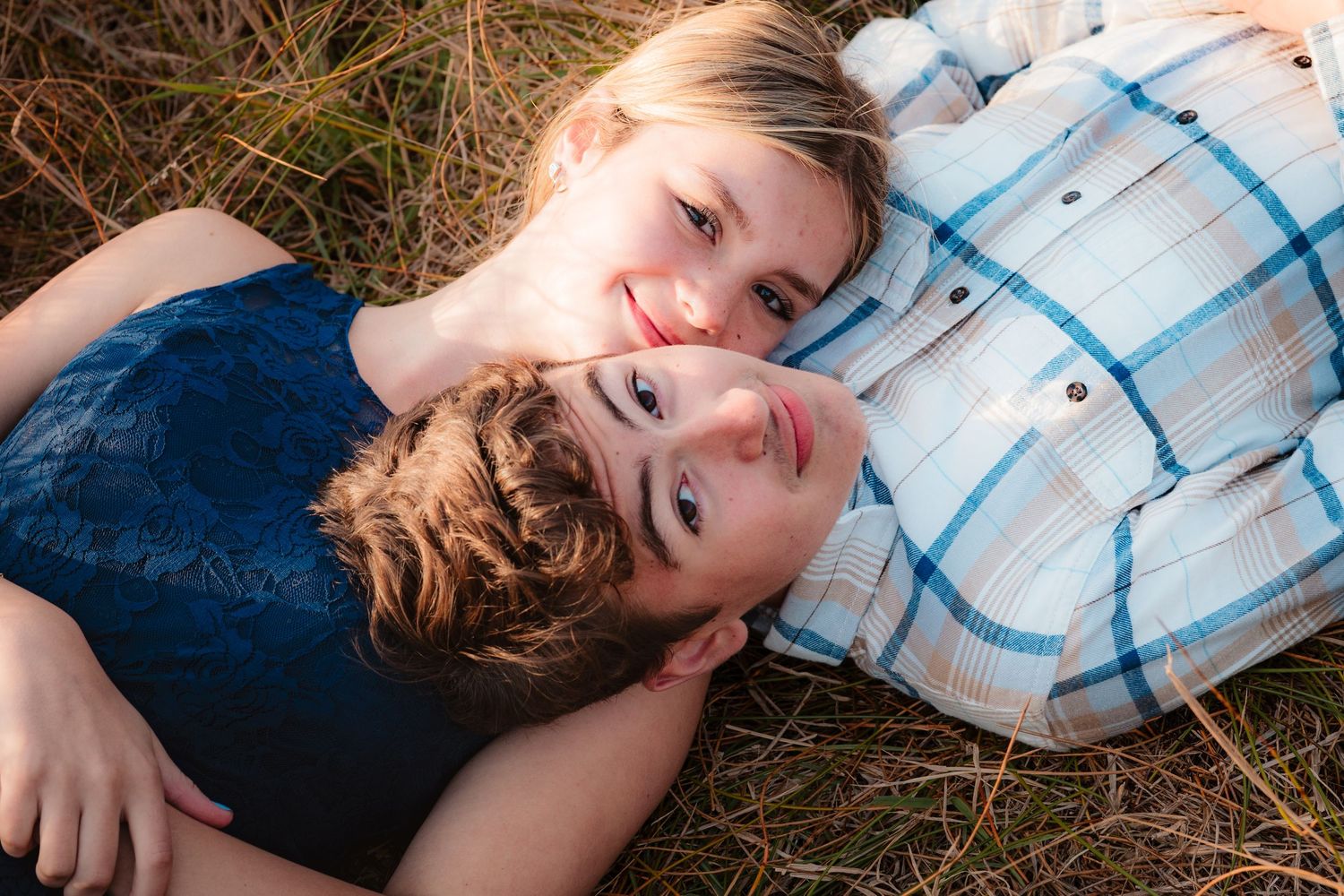 Young couple lying in the grass looking up together in a warm outdoor setting.