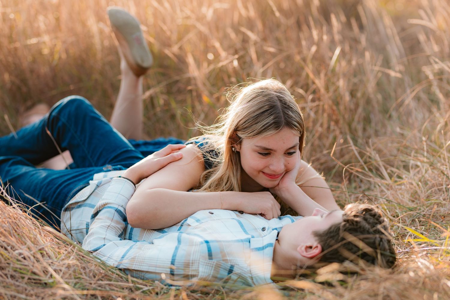 A young couple laying together in a golden grass field, woman resting her head on mans chest smiling.