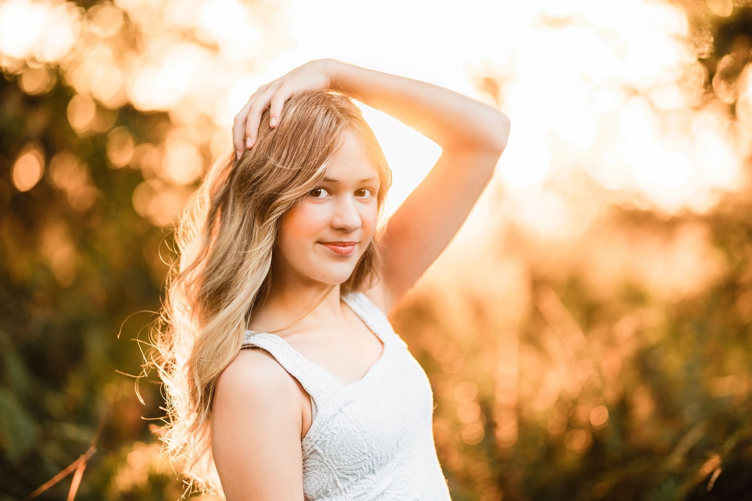 Blonde teen girl posing with arm raised in warm golden sunset light.