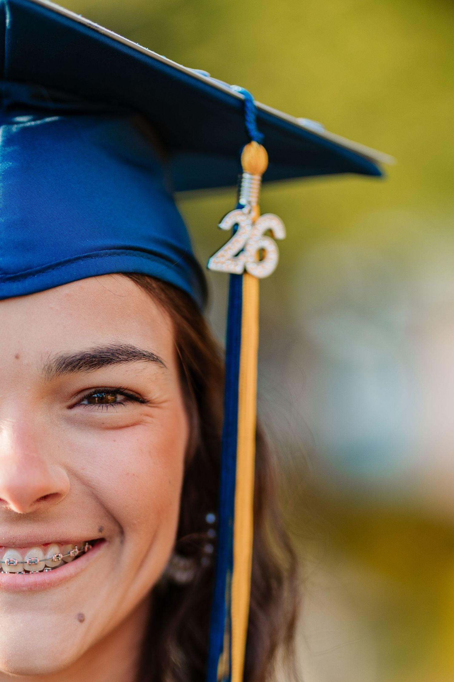 Smiling teen in blue graduation cap with '26' tassel charm, wearing braces, celebrating class of 2026.
