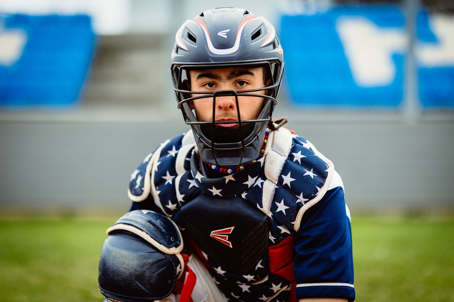 Youth baseball catcher in patriotic stars gear posing in ready stance on baseball field.