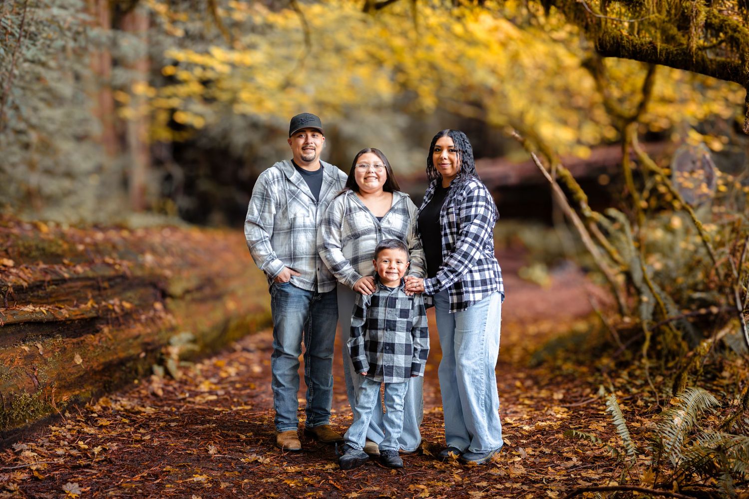 Family of four smiles together on an autumn redwood forest path surrounded by golden fall foliage.