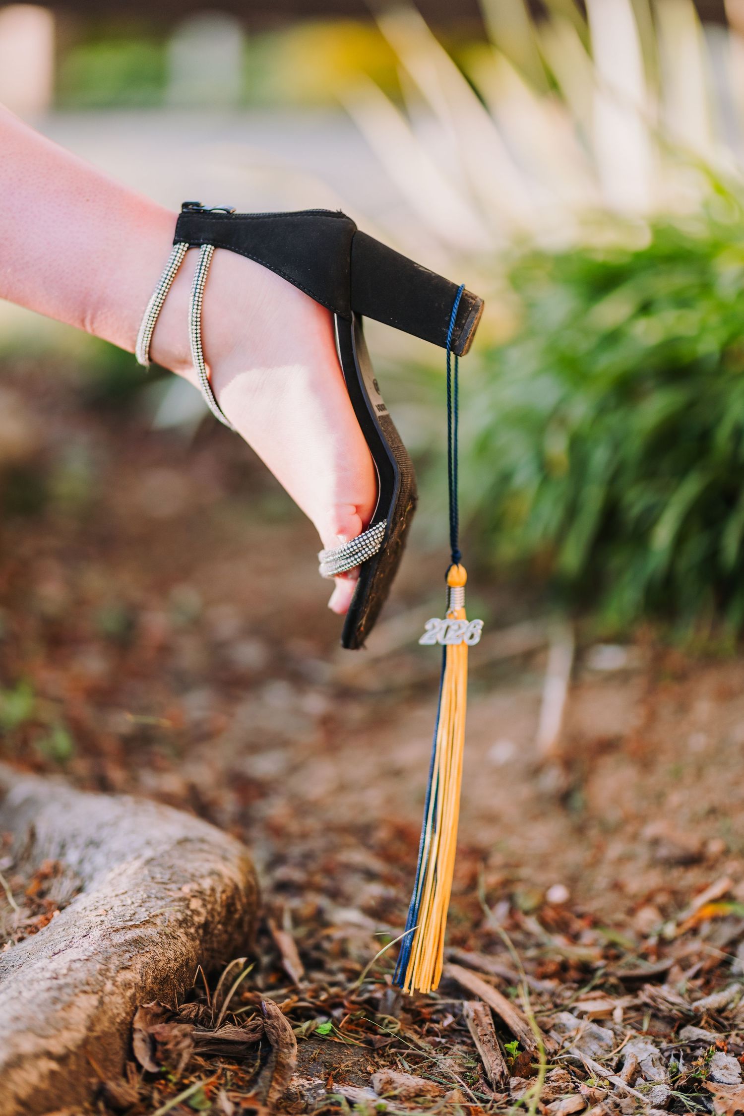 Hand holding a graduation cap tassel with 2023 charm and gold fringe outdoors.