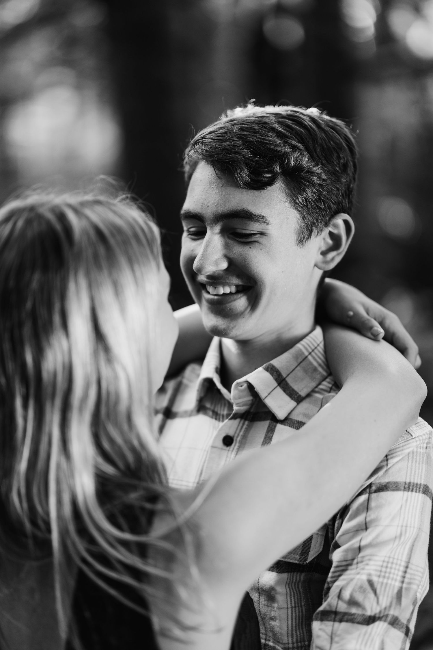 Young couple embracing and smiling at each other in a black and white romantic outdoor portrait.