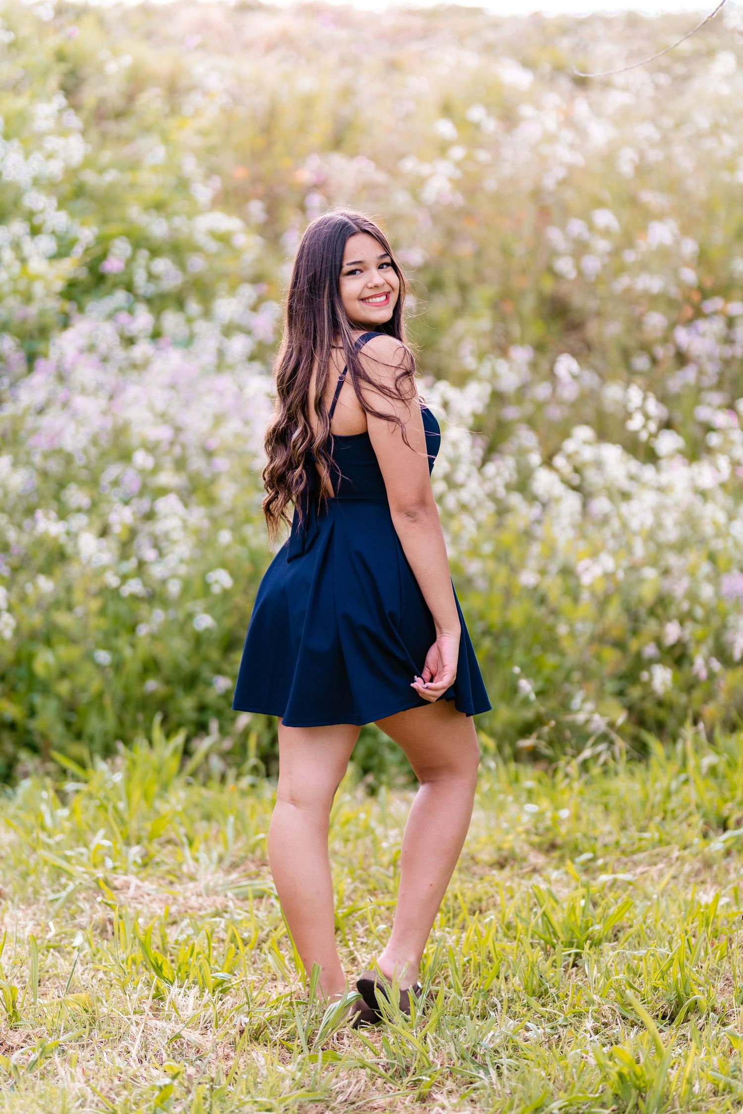 Young woman in navy blue dress smiling over shoulder in wildflower field.