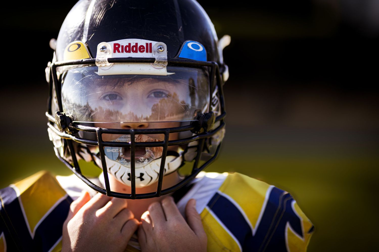 Close-up portrait of young football player fastening helmet chin strap outdoors.