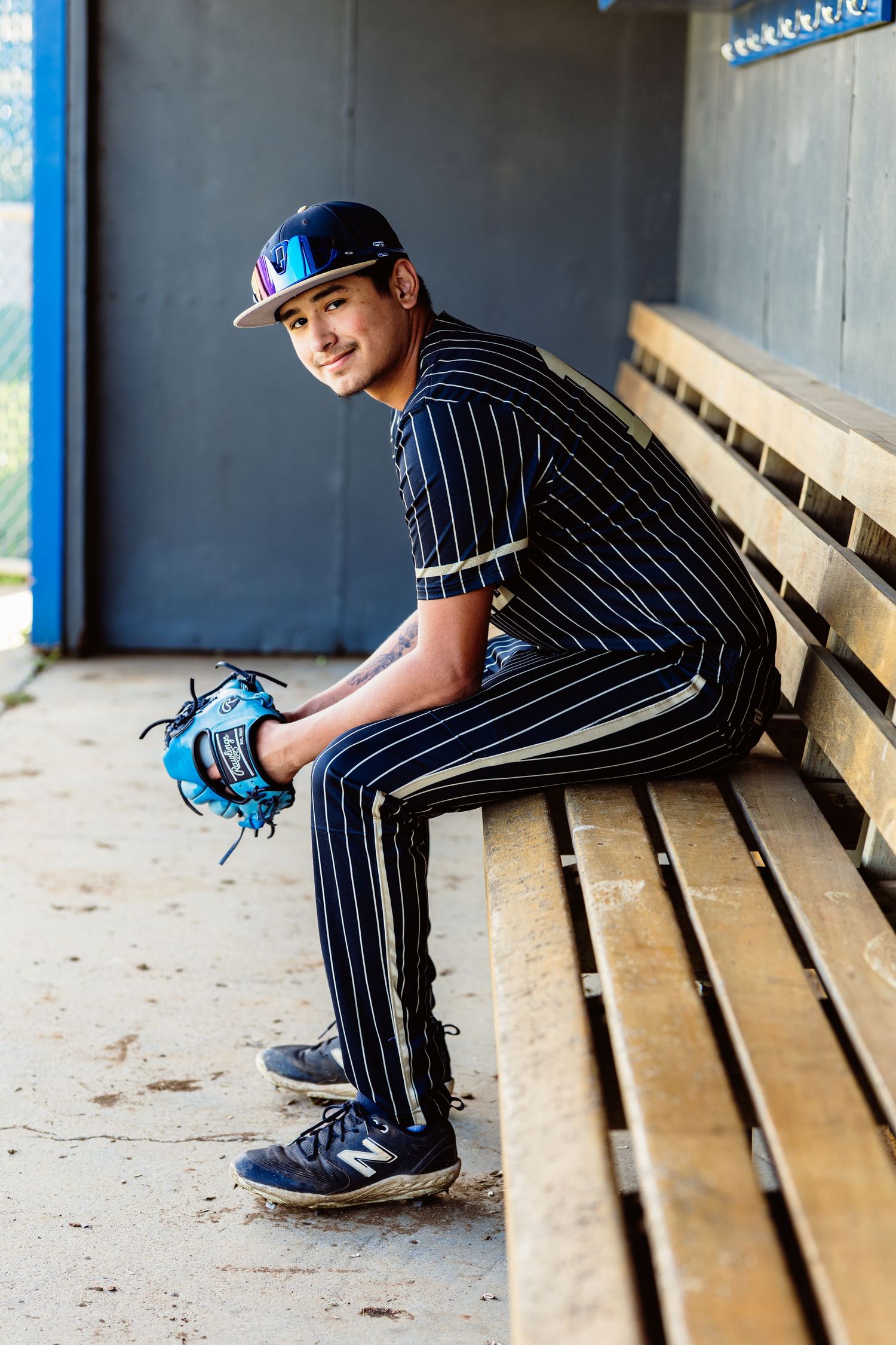 Baseball player in pinstripe uniform sits in dugout holding blue glove.