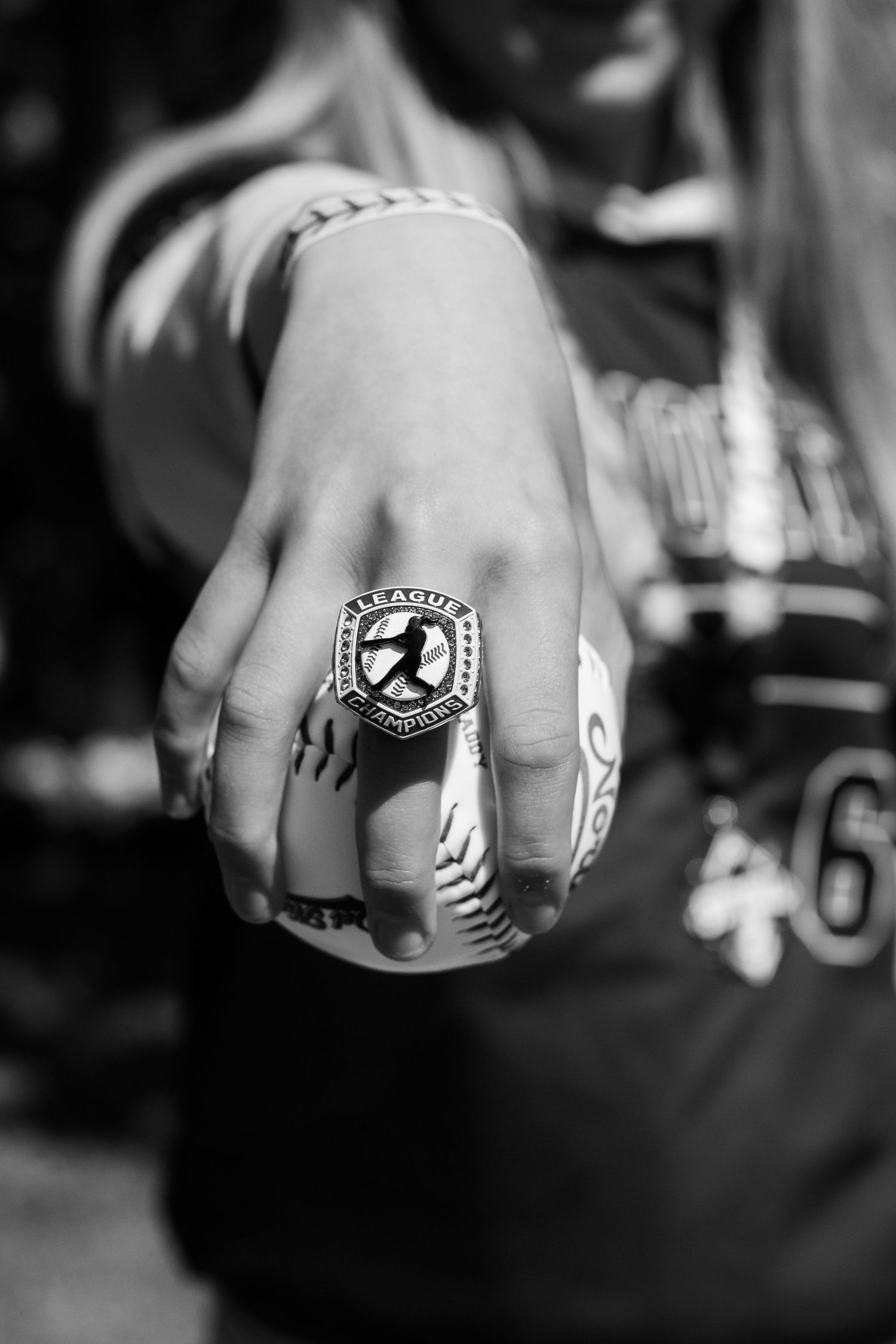 Black and white photo of a hand wearing a baseball league championship ring while gripping a baseball.