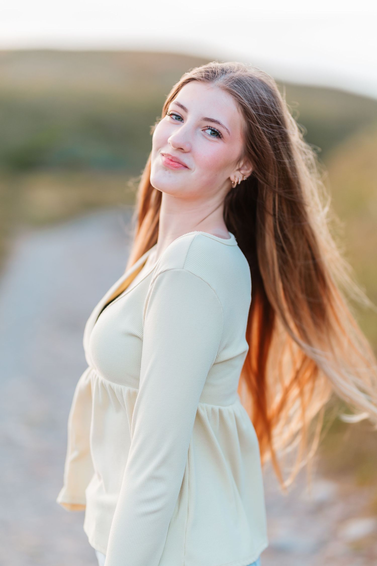Young woman with long auburn hair in cream top smiling outdoors on a windy day.