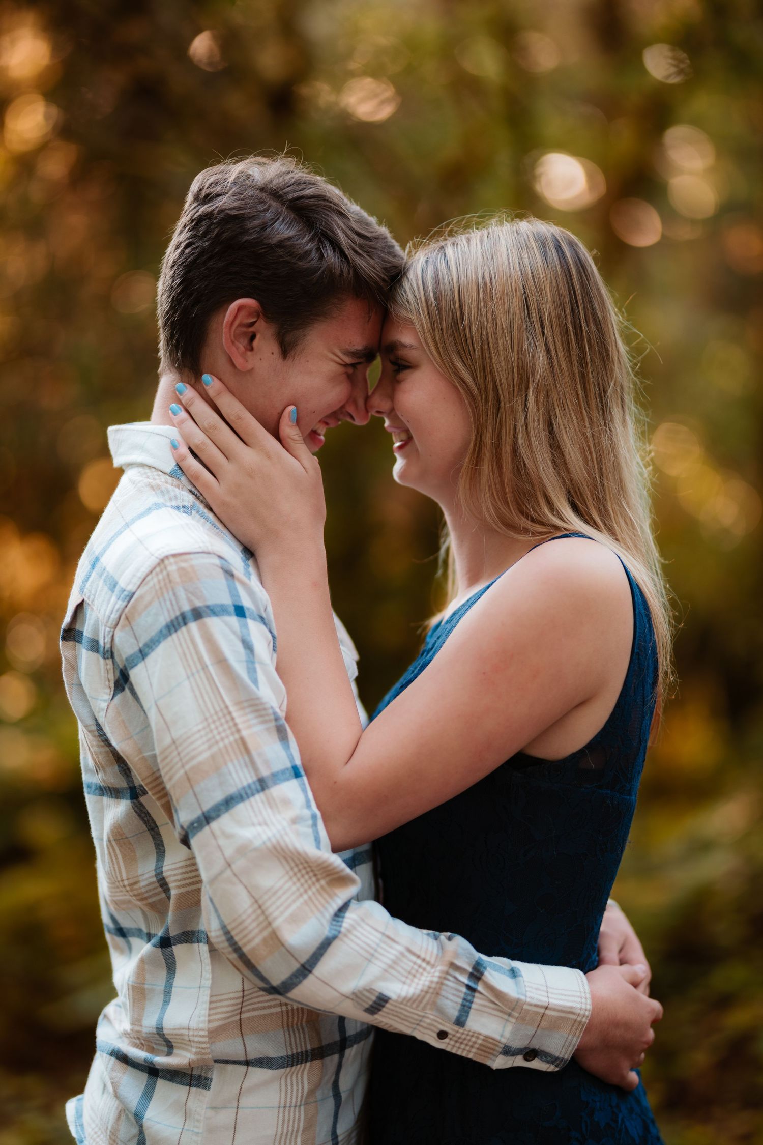 Young couple sharing a tender forehead-to-forehead moment surrounded by golden bokeh outdoors.