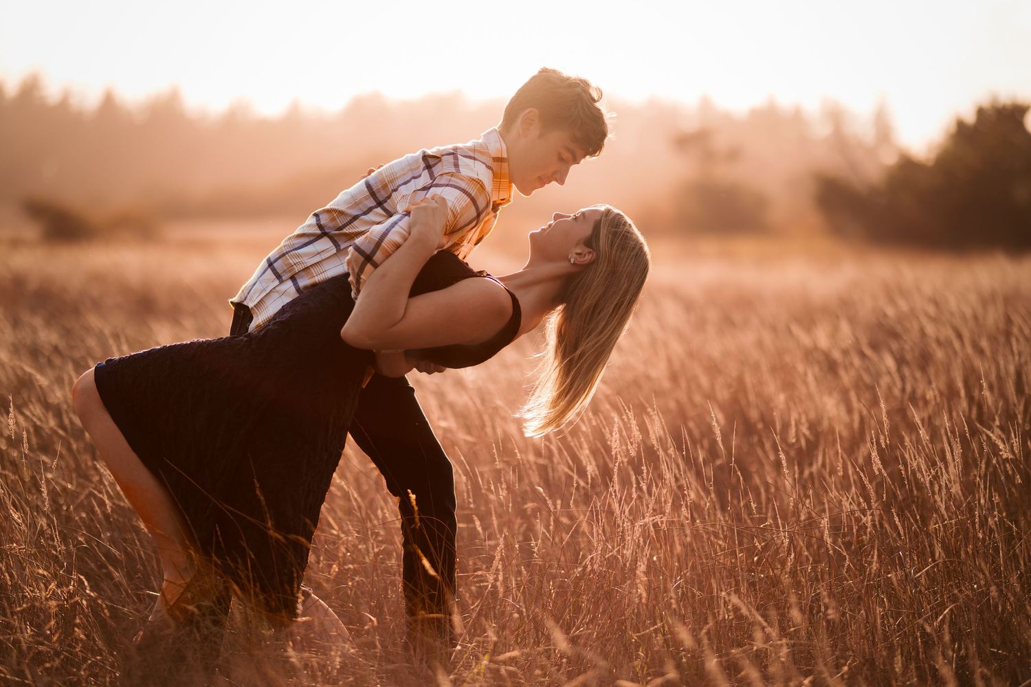 Young couple sharing a romantic dip kiss in a warm golden wheat field at sunset.