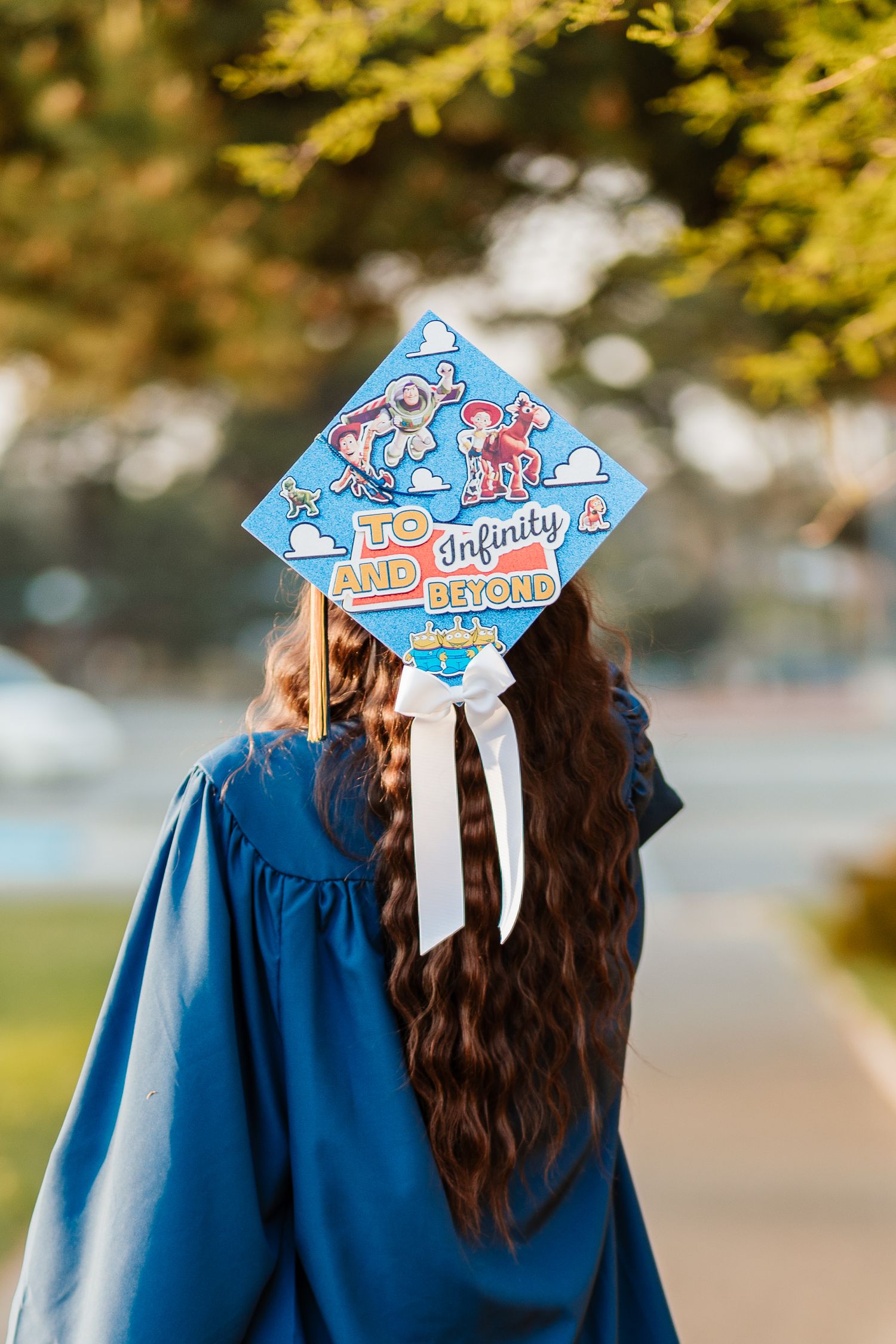 Graduate in blue gown wearing decorated Toy Story graduation cap reading To Infinity and Beyond outdoors.