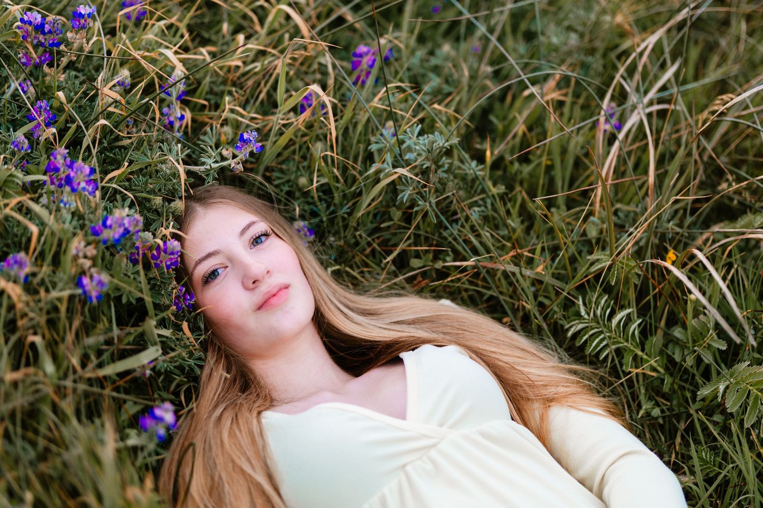 Young woman with long blonde hair lying among purple wildflowers in a lush field.