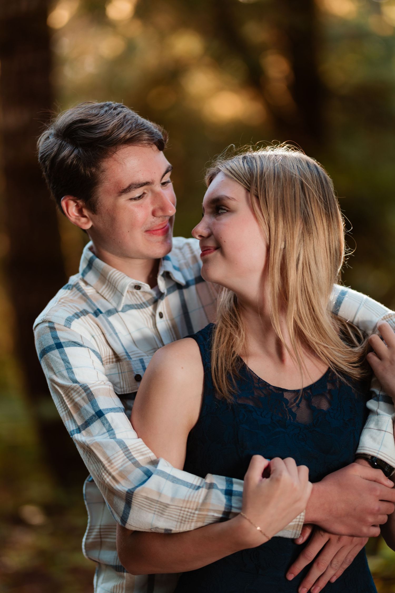 Young couple embracing and gazing at each other romantically in sunlit forest setting.