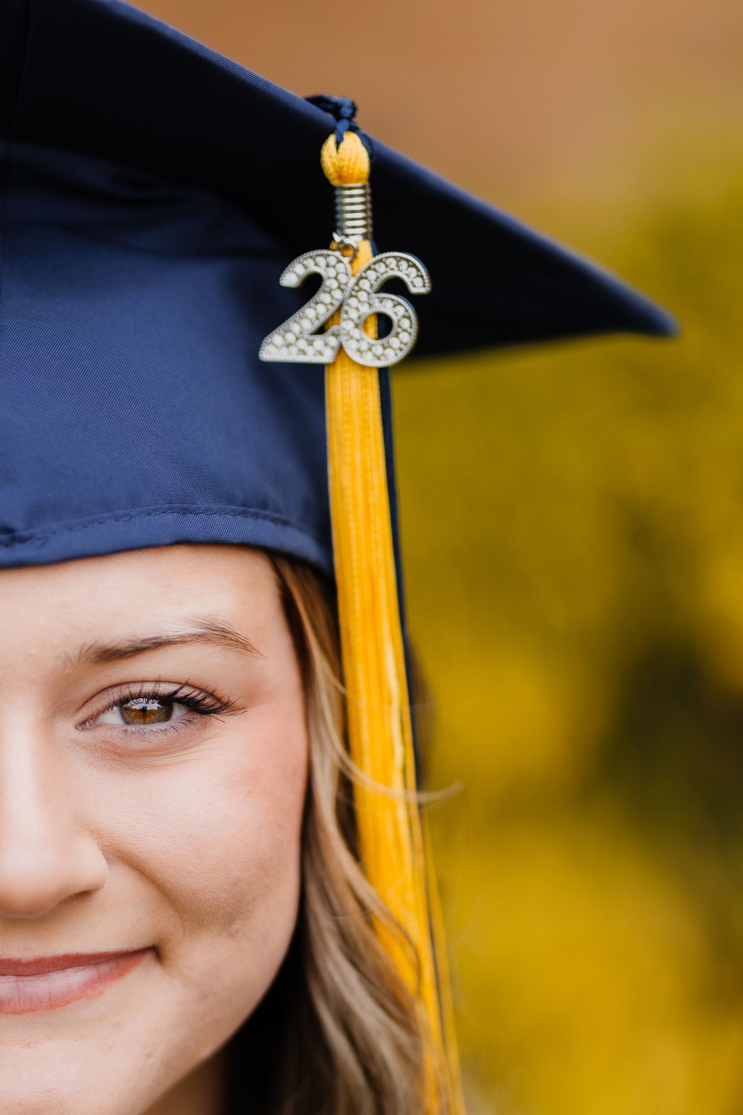 A smiling young woman wearing a navy blue graduation cap with a gold tassel and sparkly '26' charm for the class of 2026.