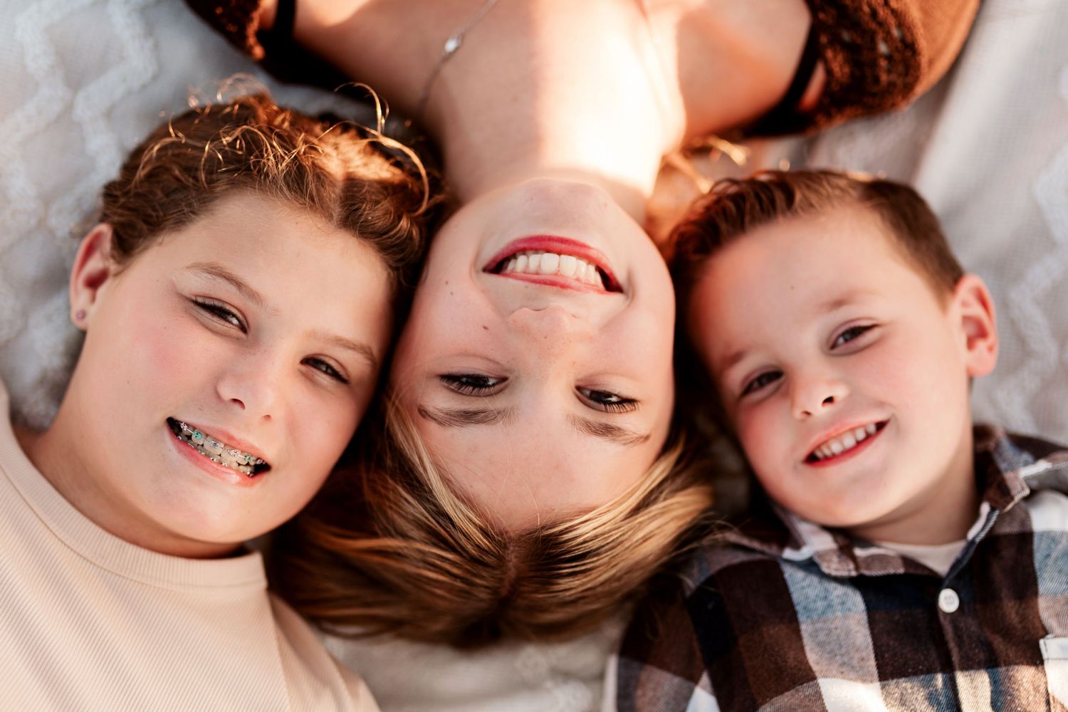 Three smiling children lying down together, two boys and a girl, posing for a cheerful portrait photo.