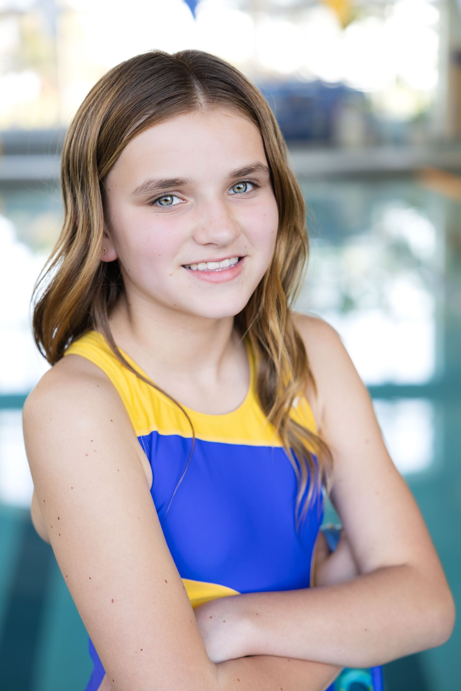 Smiling young girl in blue and yellow swimsuit poses at indoor pool.