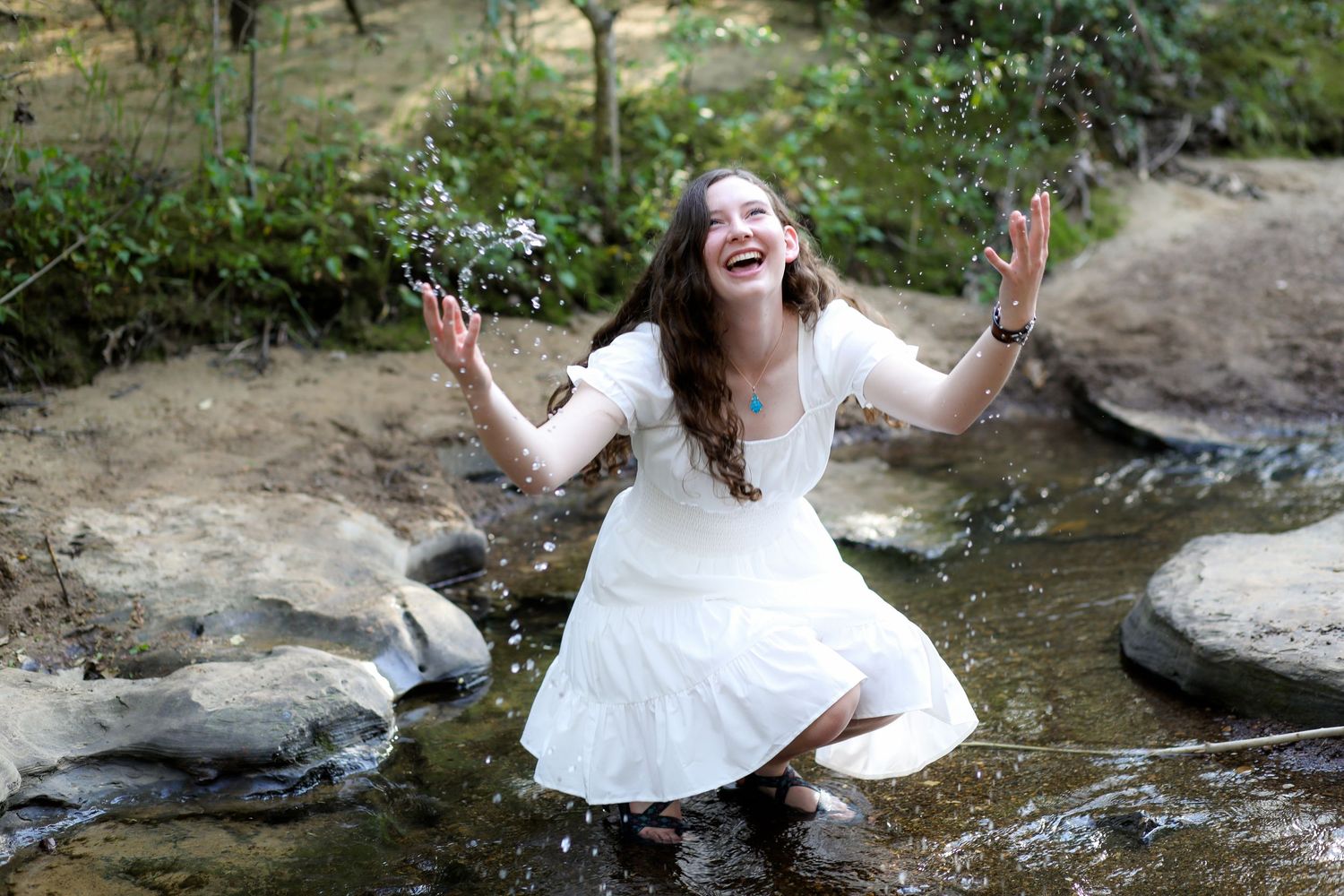 A joyful moment captured in white dress by a stream with arms outstretched in pure delight.