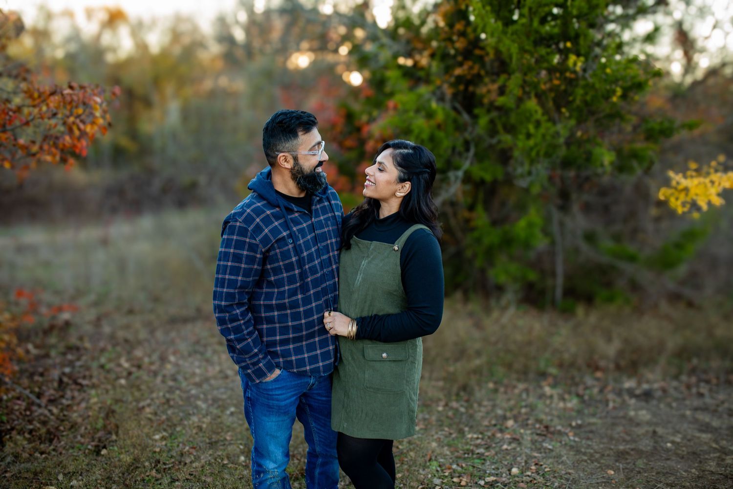 A couple in casual fall clothing share an intimate moment while standing together on a leaf-covered autumn path.