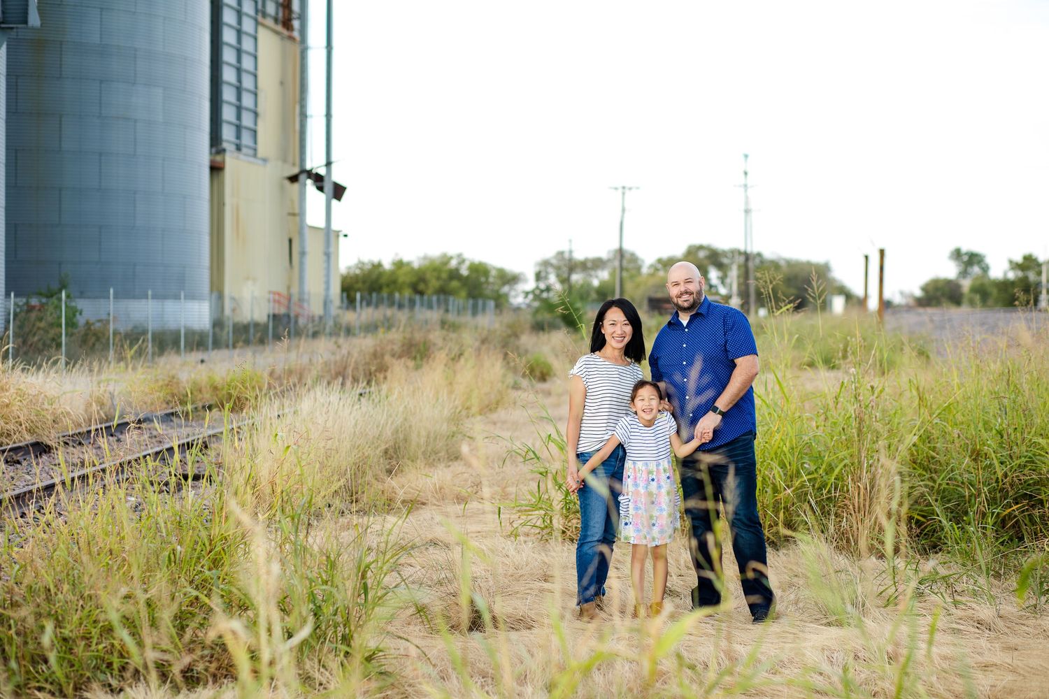 Parent and children walking together through a tall grassy field during golden hour at sunset.