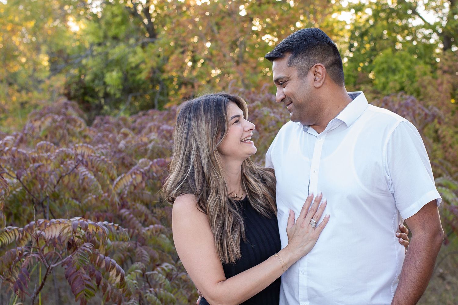A loving couple shares a romantic moment outdoors in front of purple fall foliage during sunset.