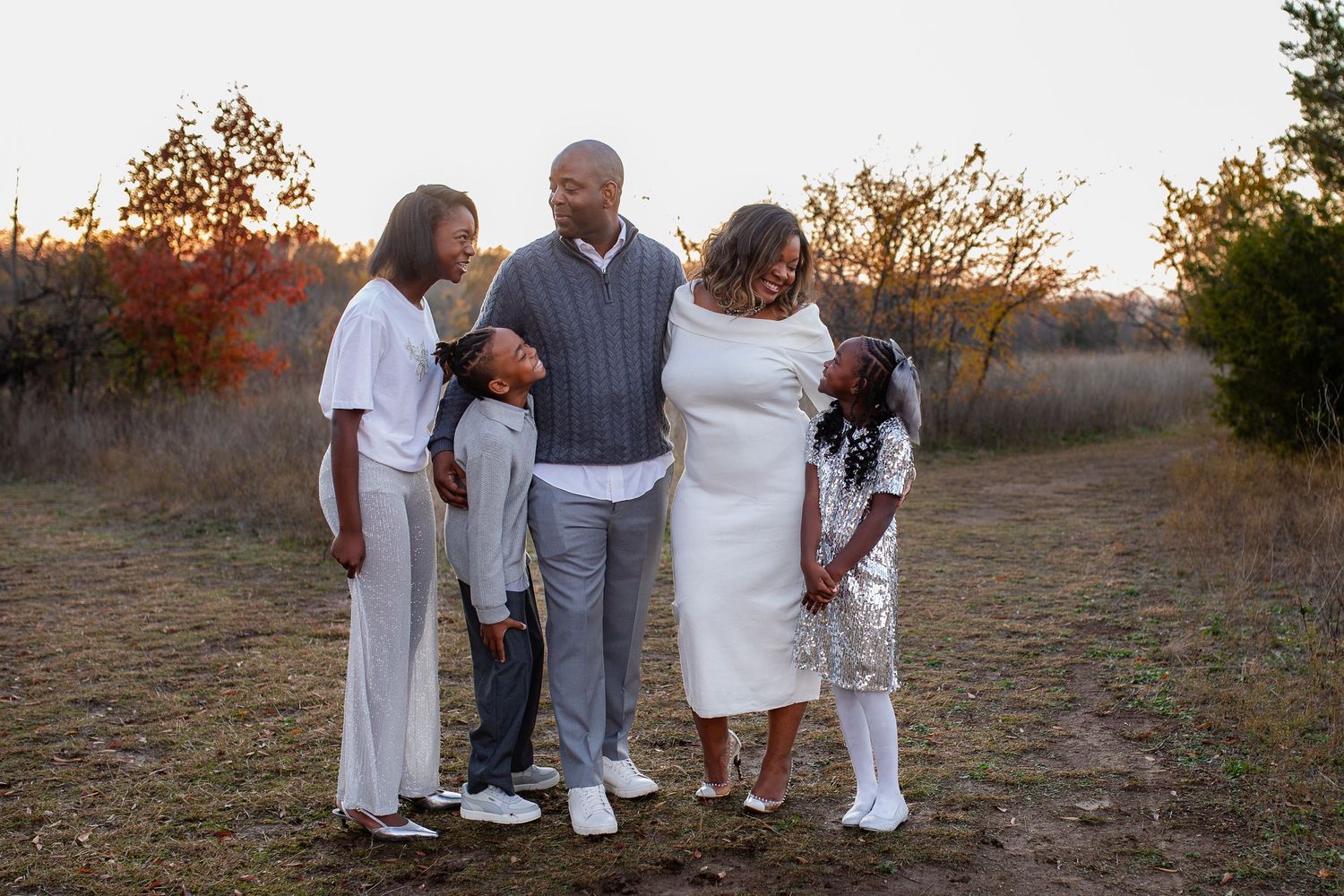 A family of five stands together in casual attire against a natural outdoor backdrop at sunset.
