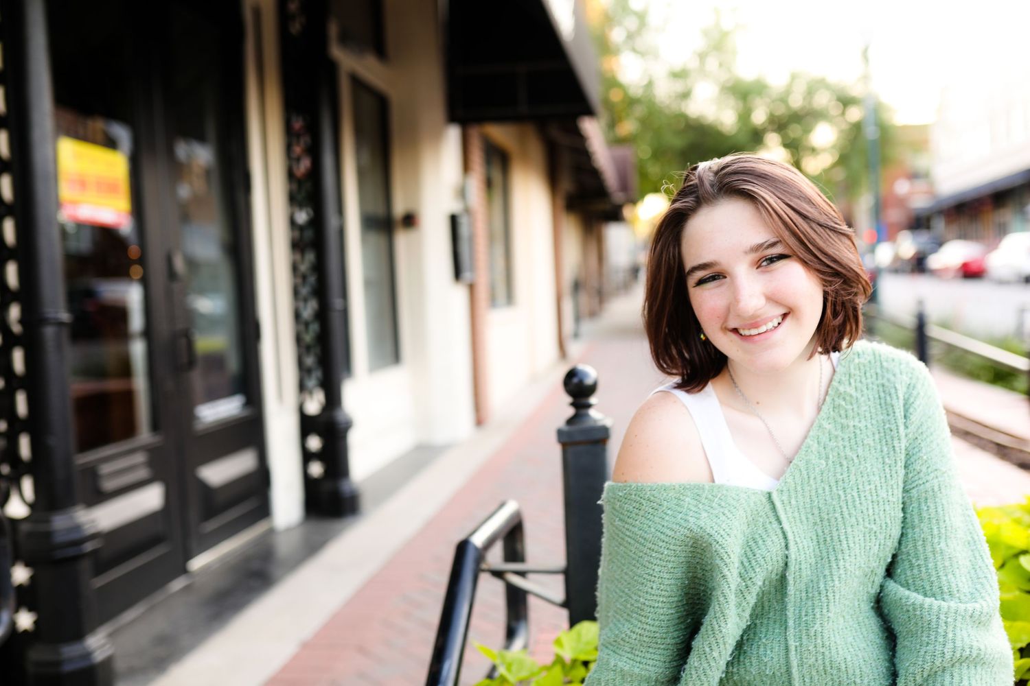 Smiling woman with short brown hair in a green sweater is photographed against a blurred outdoor background.