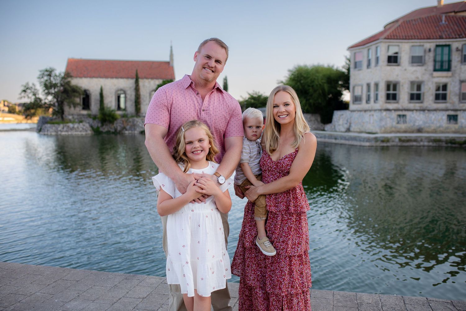 A family poses together on a pier near a waterfront with houses and buildings visible in the background.