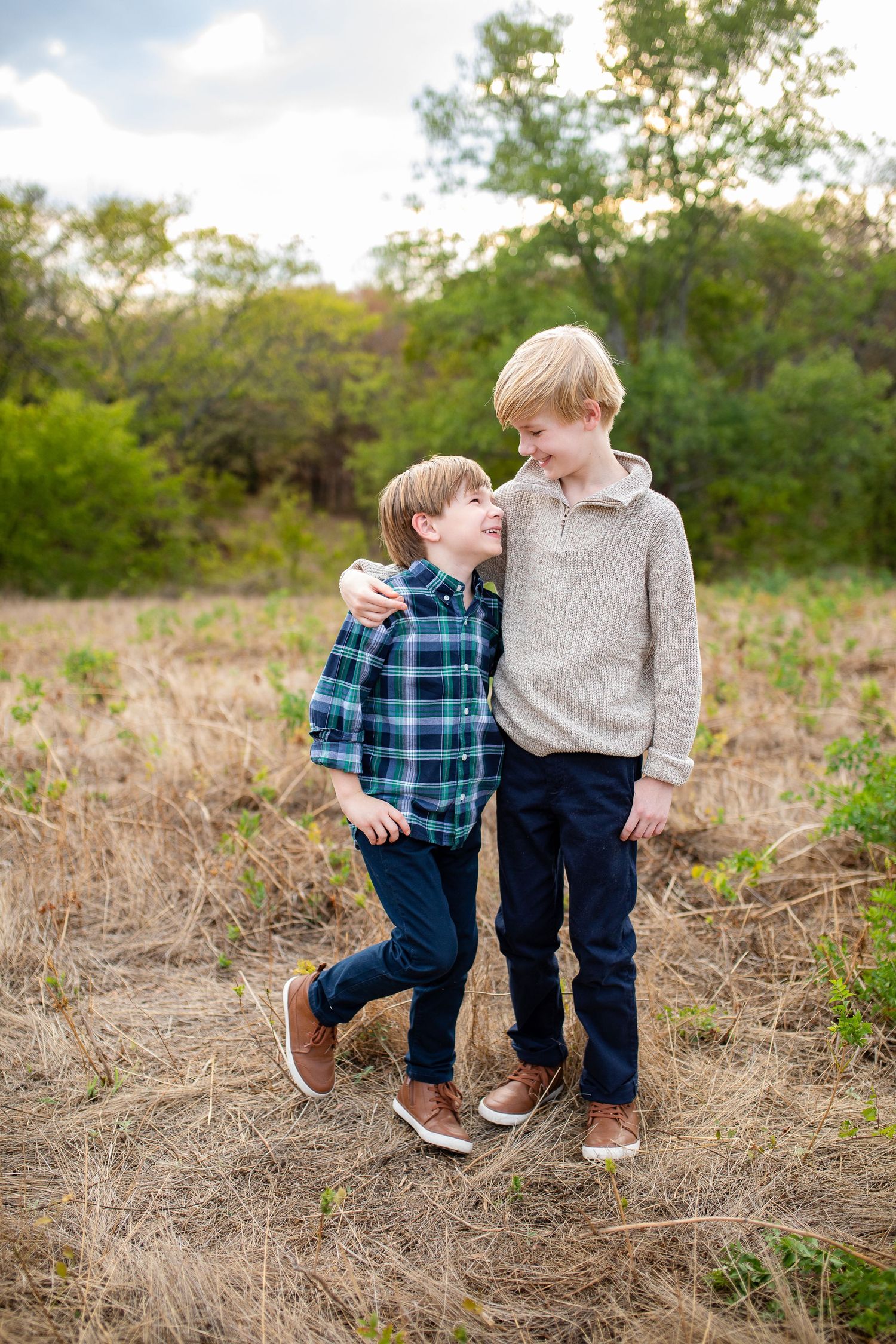 Two children walk together through a golden dry grass field on an autumn afternoon.