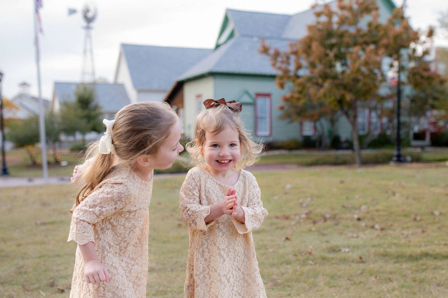 Two children in lace dresses share a joyful moment while playing together in a grassy field.