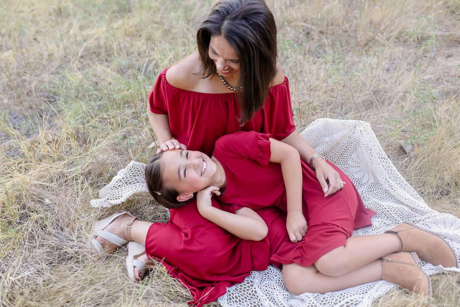 A series of romantic outdoor maternity photos showing a woman in a red dress posing on a blanket in a grassy field.