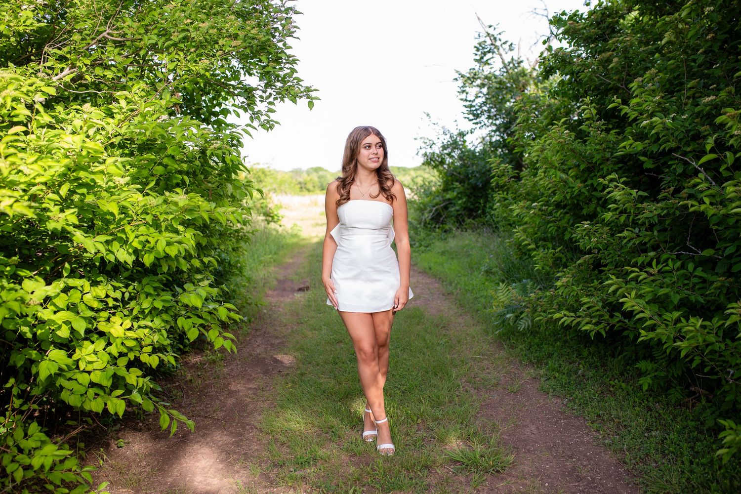 A person walks along a serene nature trail surrounded by lush green foliage in summer.