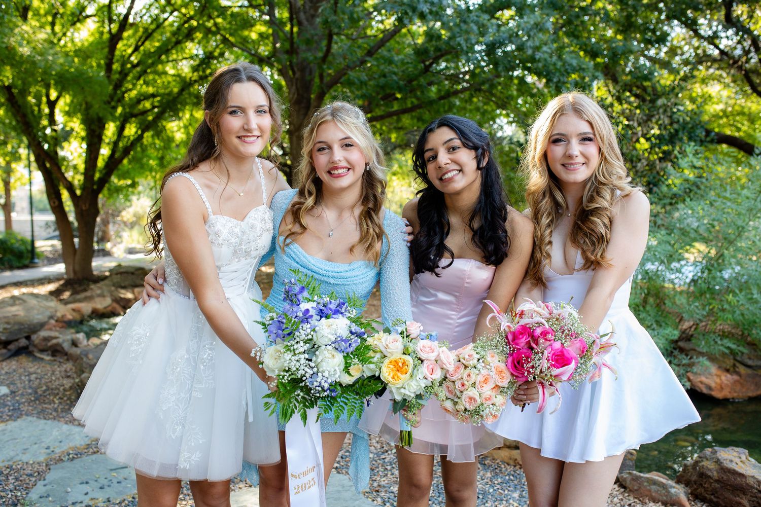 People dressed in white gather outdoors near trees for a celebratory outdoor photo session.