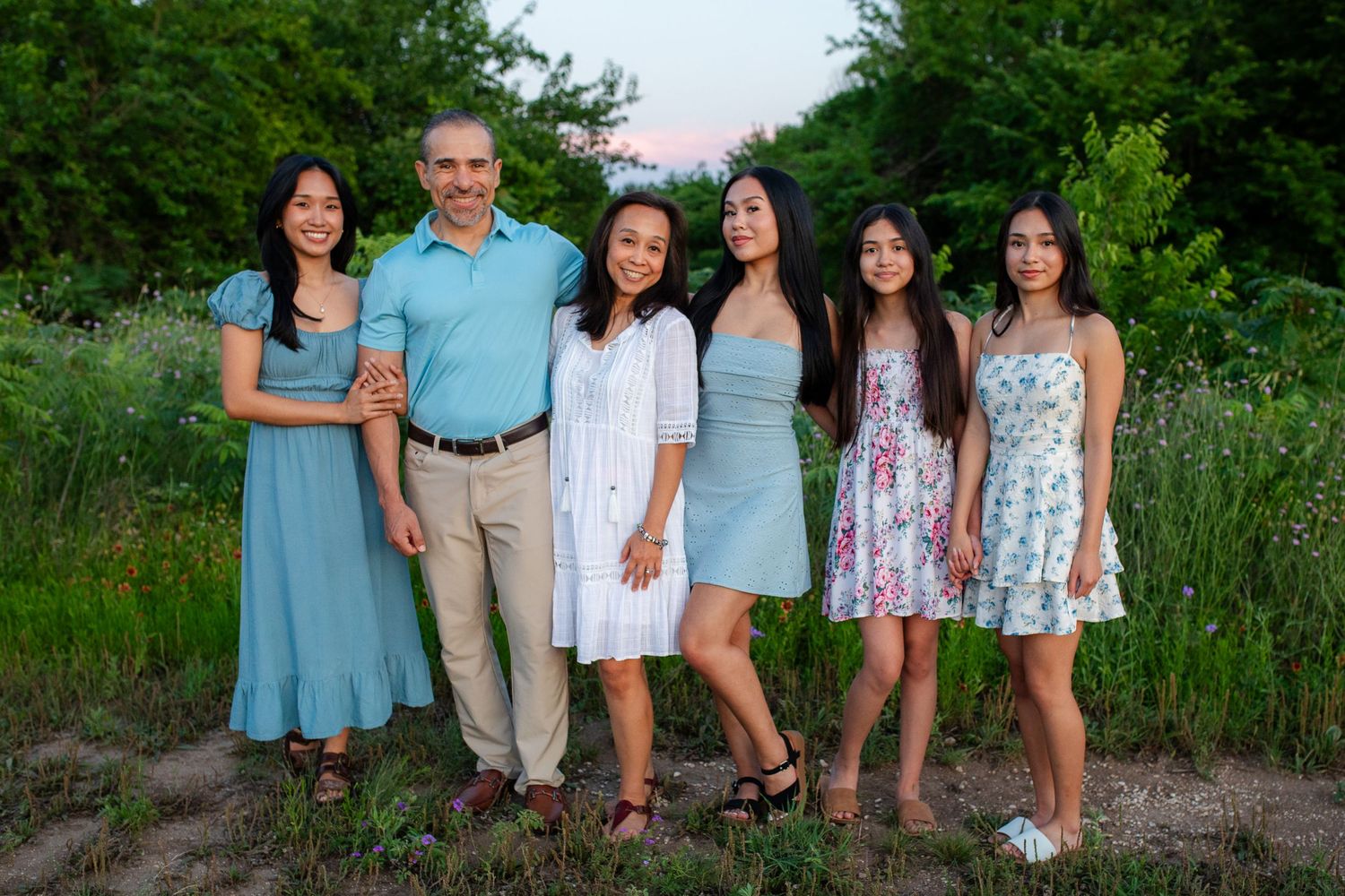 Extended family wearing coordinated blue and white outfits poses together for outdoor portrait session in nature setting.