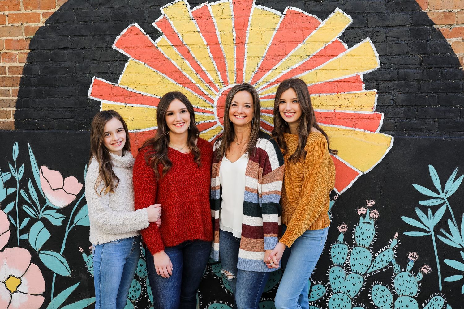 A group of people standing against a colorful mural wall with sunburst patterns and teal floral designs.