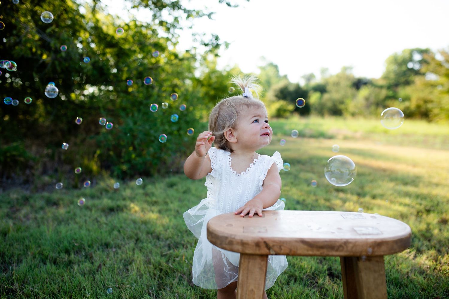 A laughing child plays outdoors near bubbles in a golden-lit garden setting during sunset.