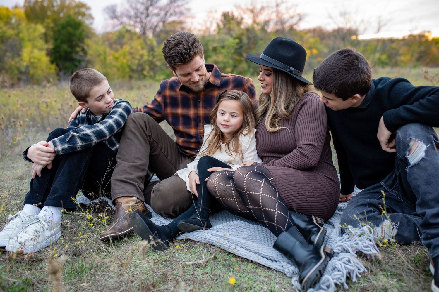 Group of people relaxing and sitting together on grassy ground in warm autumn sunlight during outdoor gathering.
