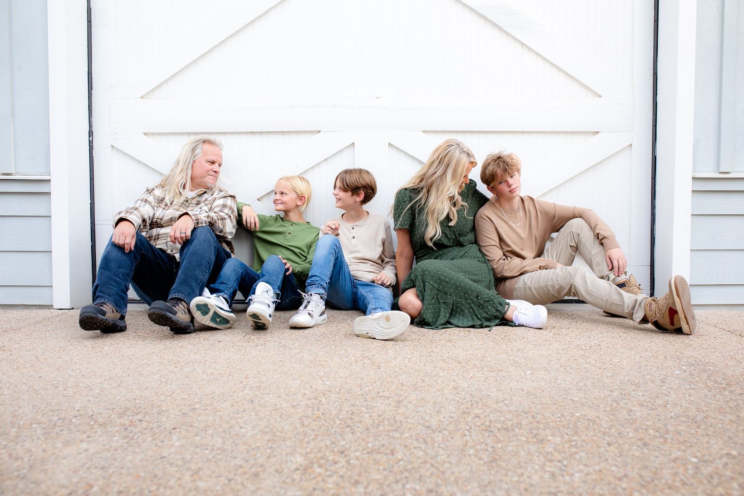 Five people sit casually together on floor against white door wearing coordinating outfits in light neutral colors.