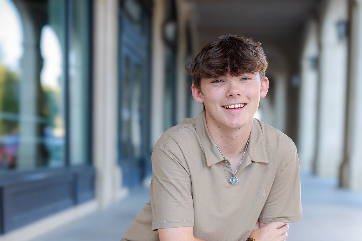 A smiling person in a beige polo shirt stands in a bright, modern indoor hallway.